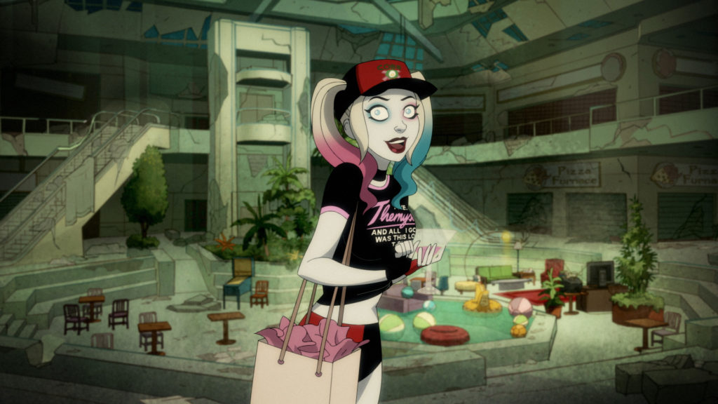Harley Quinn is back at the hideout, wearing a Cobb Squad shirt, a shirt saying "I went to Themyscira, and all I got was this lousy t-shirt," and drinking from a martini glass.