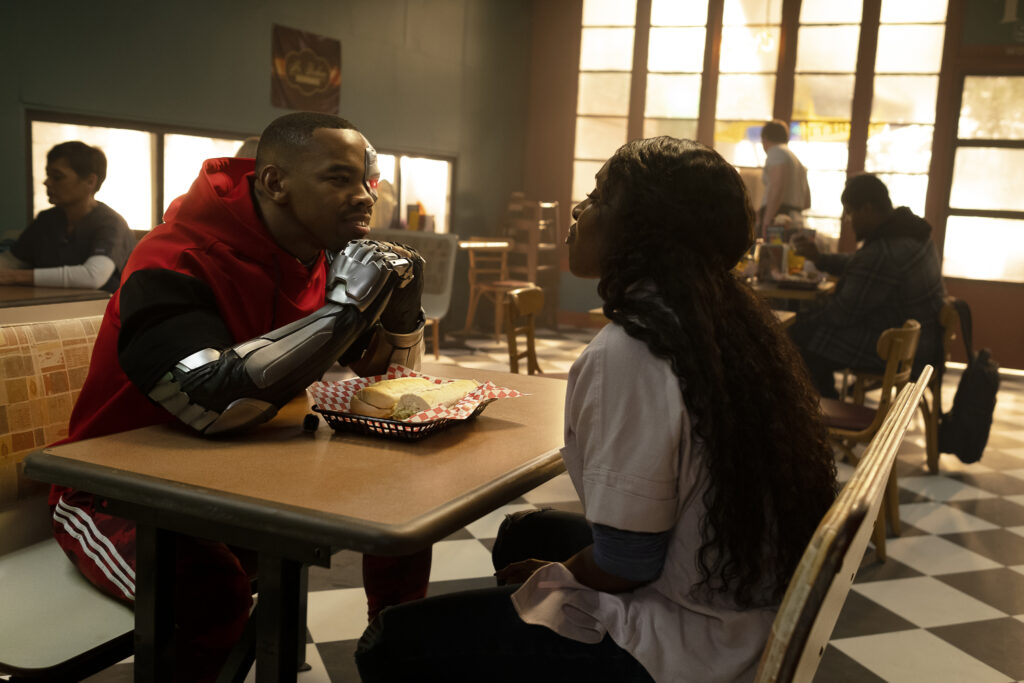 Left to Right: Joivan Wade as Vic Stone/Cyborg and Karen Obilom as Roni Evers having lunch at a sub shop.