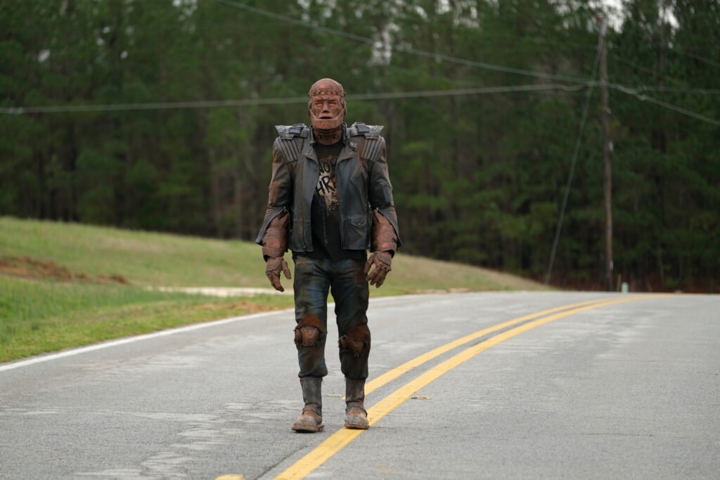 Cliff (Riley Shanahan) is walking in the middle of the road in the middle of the country.