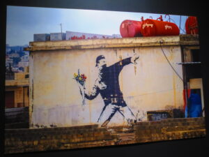 “Love is in the Air (Flower Thrower)” Stencil on Palestinian Wall of a masked young man throwing a bouquet of flowers