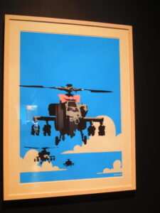 Happy Choppers by Banksy. Stenciled Helicopters in the sky with a pink ribbon beneath the blades