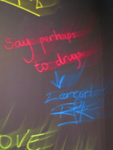 On Chalkboard, in red “Say perhaps to drugs” then in blue with an arrow pointing down it says “I concur! RJK”