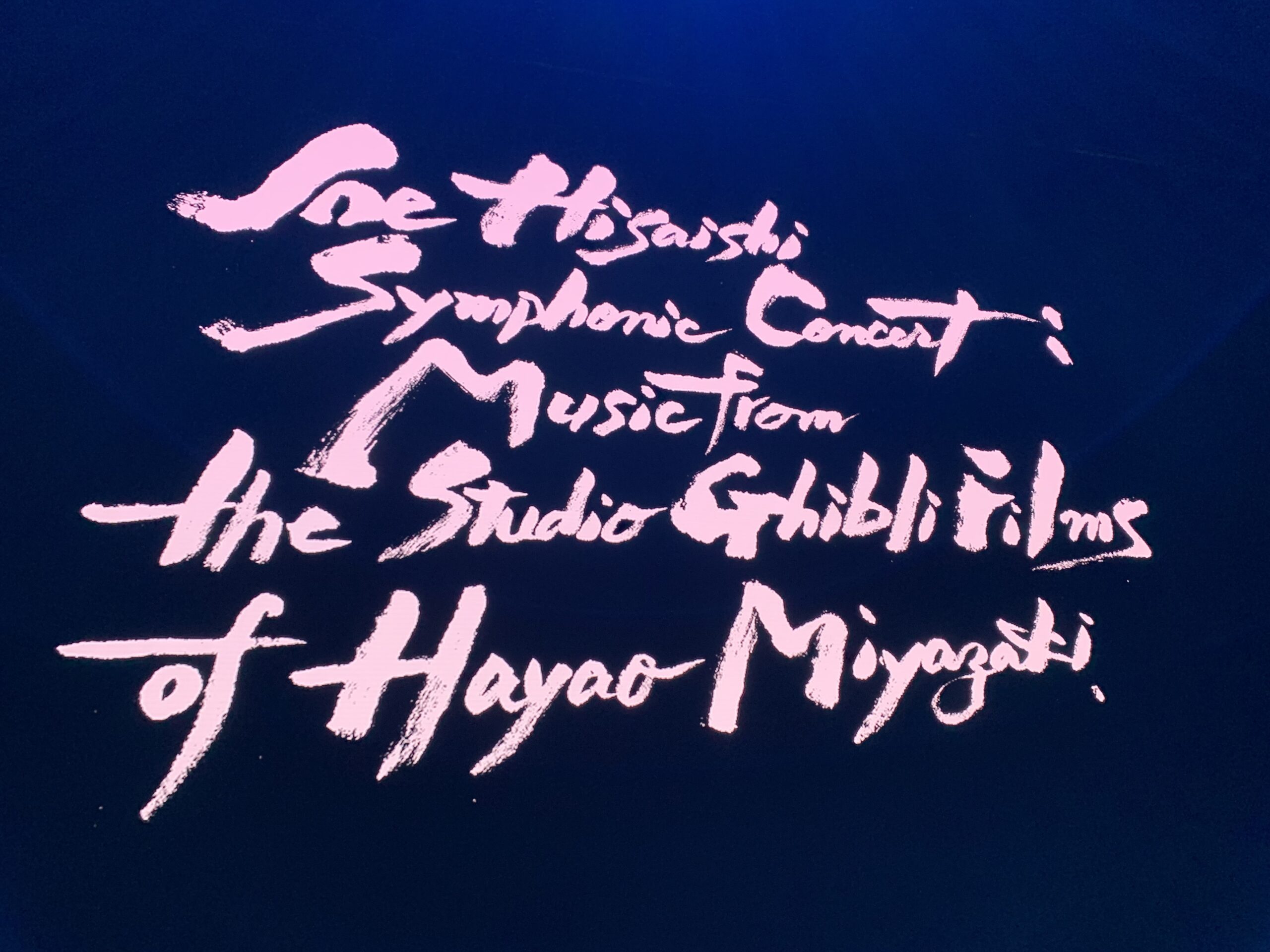 Black screen with pink letters that say Joe Hisaishi Symphonic Concert: Music from the Studio Ghibli Films of Hayao Miyazaki