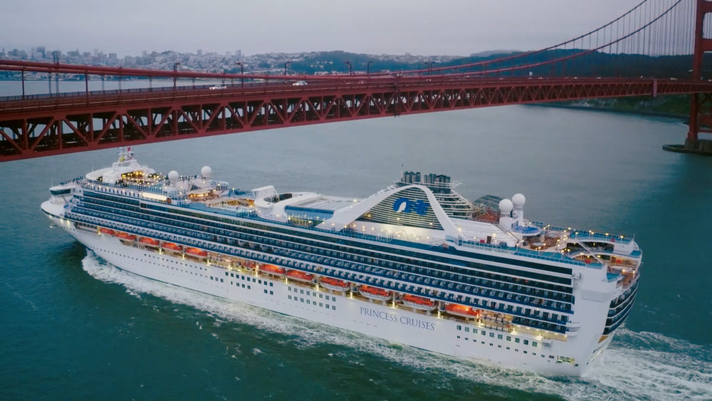 Screenshot from Hell of a Cruise, of a cruise ship out in the water below a long red bridge.