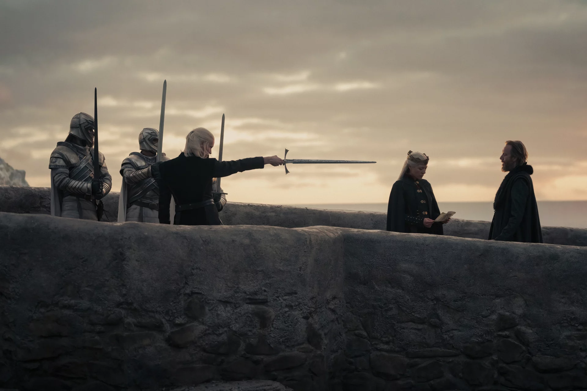 Daemon points the tip of his blade at Otto Hightower on the bridge of Dragonstone. As Rhaenyra Targaryen reads a letter from King's Landing 