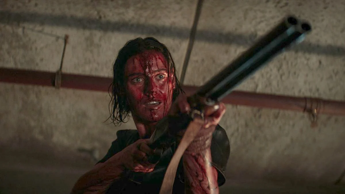 Screenshot of Lily Sullivan as Beth covered in blood and wielding a shotgun in Evil Dead Rise